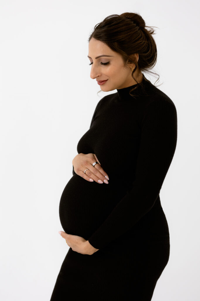 Pregnant woman with a low loose bun, lovingly holding her baby bump