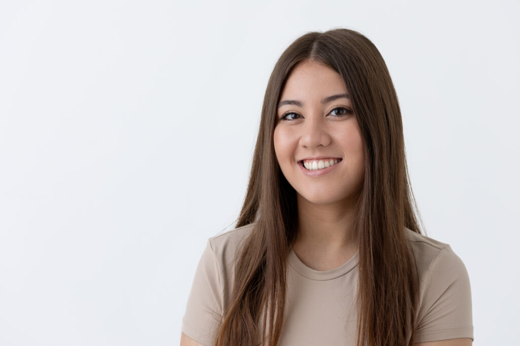 Pro headshots young lady with medium brown, long, straight hair, smiling off center right with a white background
