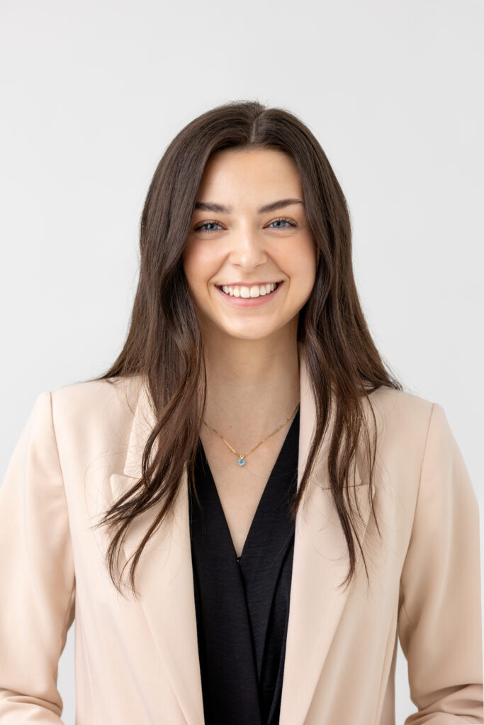 Professional Headshot of young lady with long curled brown hair, beige blazer and black blouse