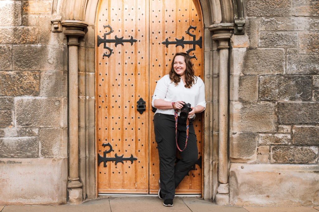 Molly leaning on an old doorway in Edinburgh holding her camera and smiling off to the right. Photo taken by Ben Shakespeare of Islay