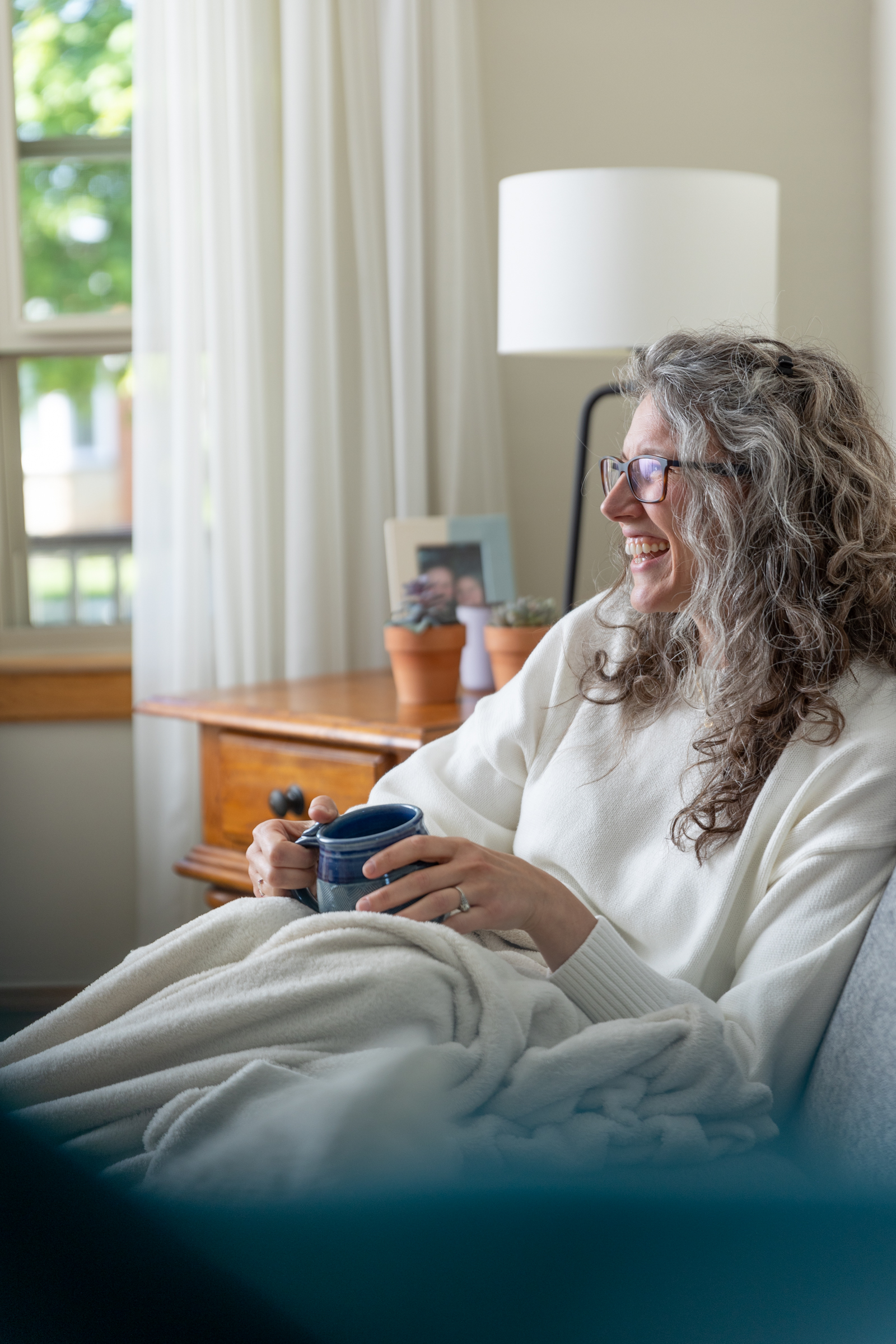 woman sitting on couch laughing with a mug in her hand 