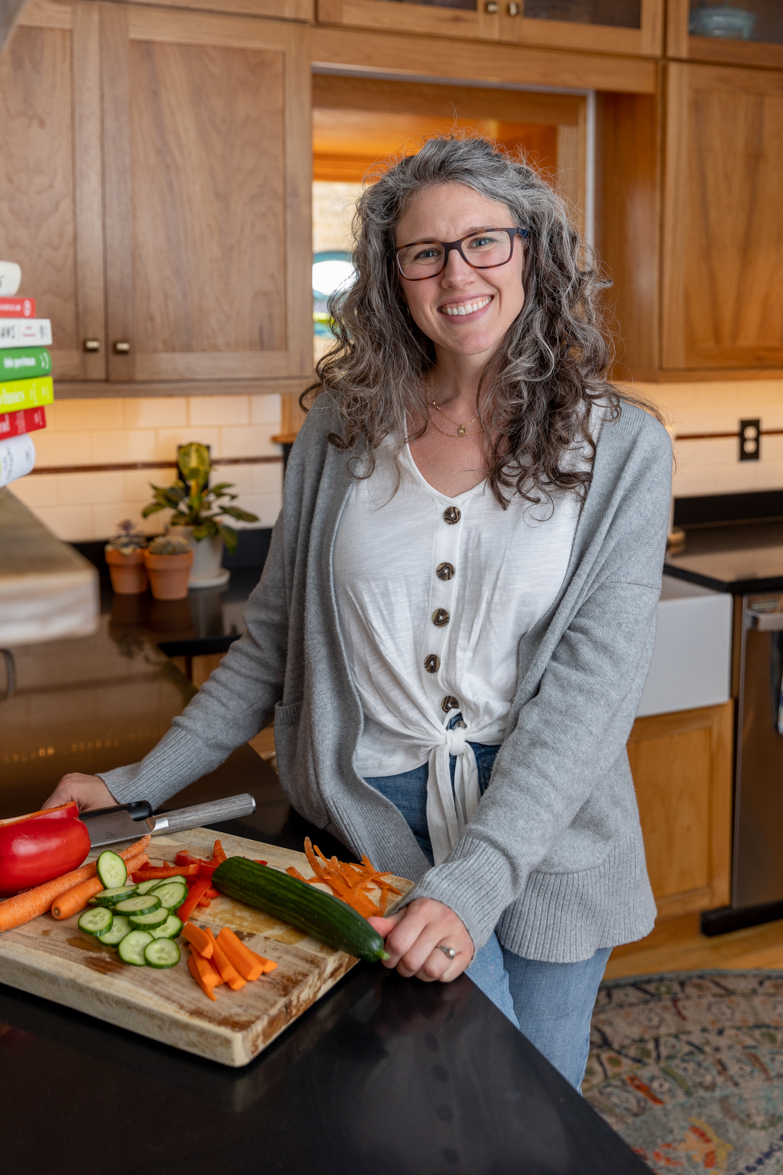 woman in a kitchen with a cutting board in front of her that has vegetables on it 