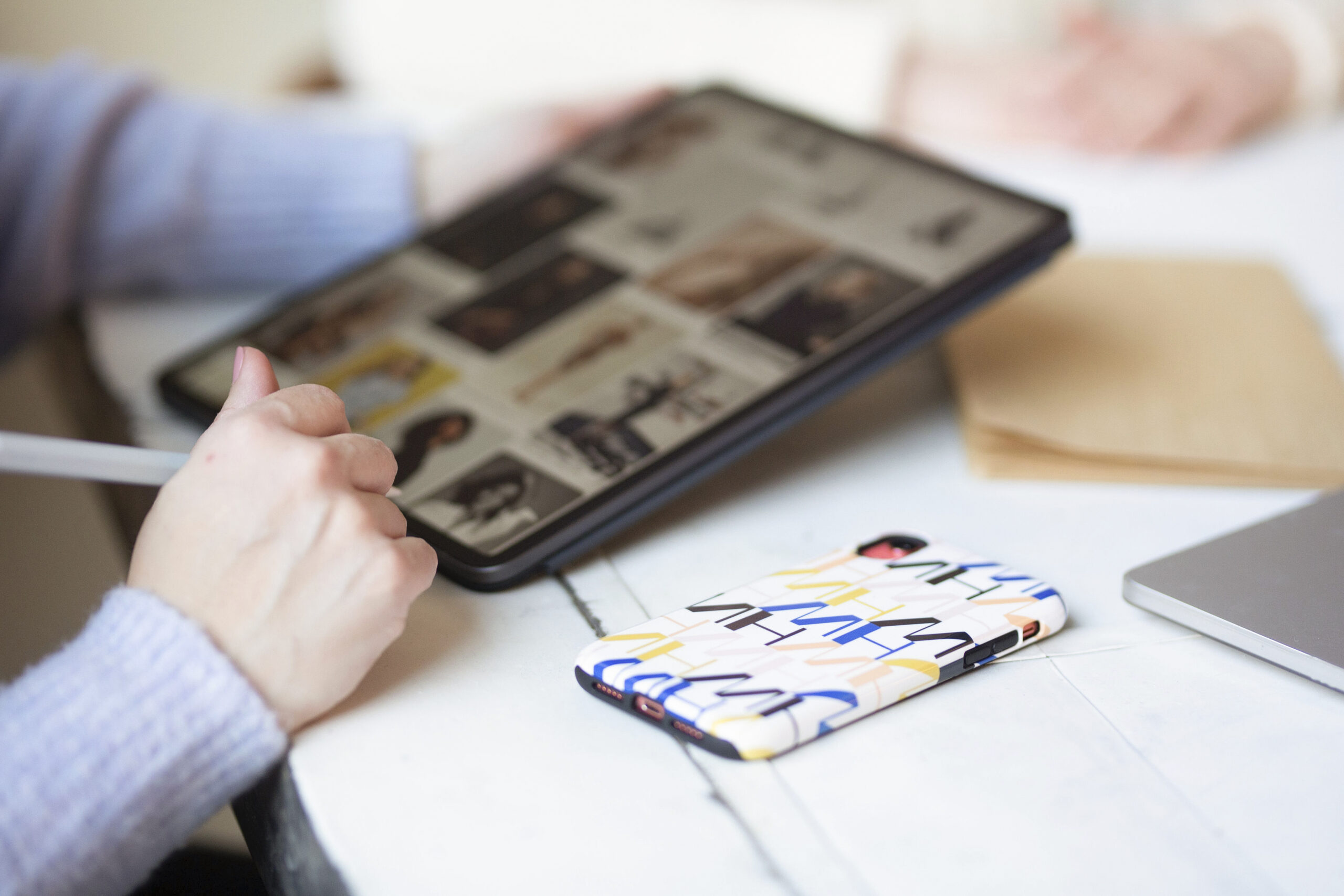 a table with a phone, notebook, and a woman holding a stylus looking at an ipad