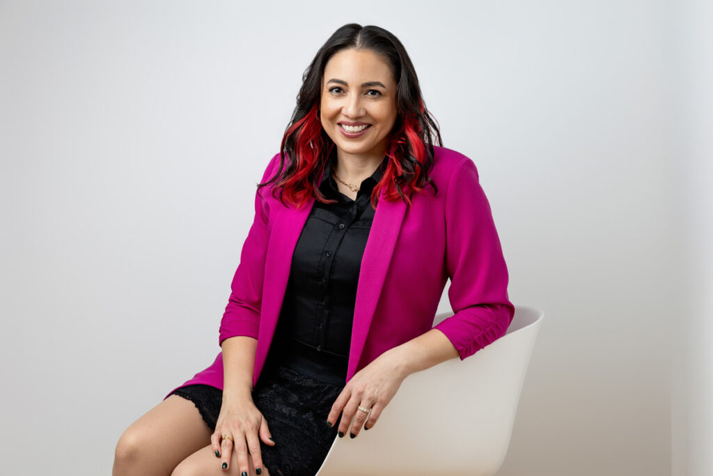 A person in a pink blazer sitting in a chair. 