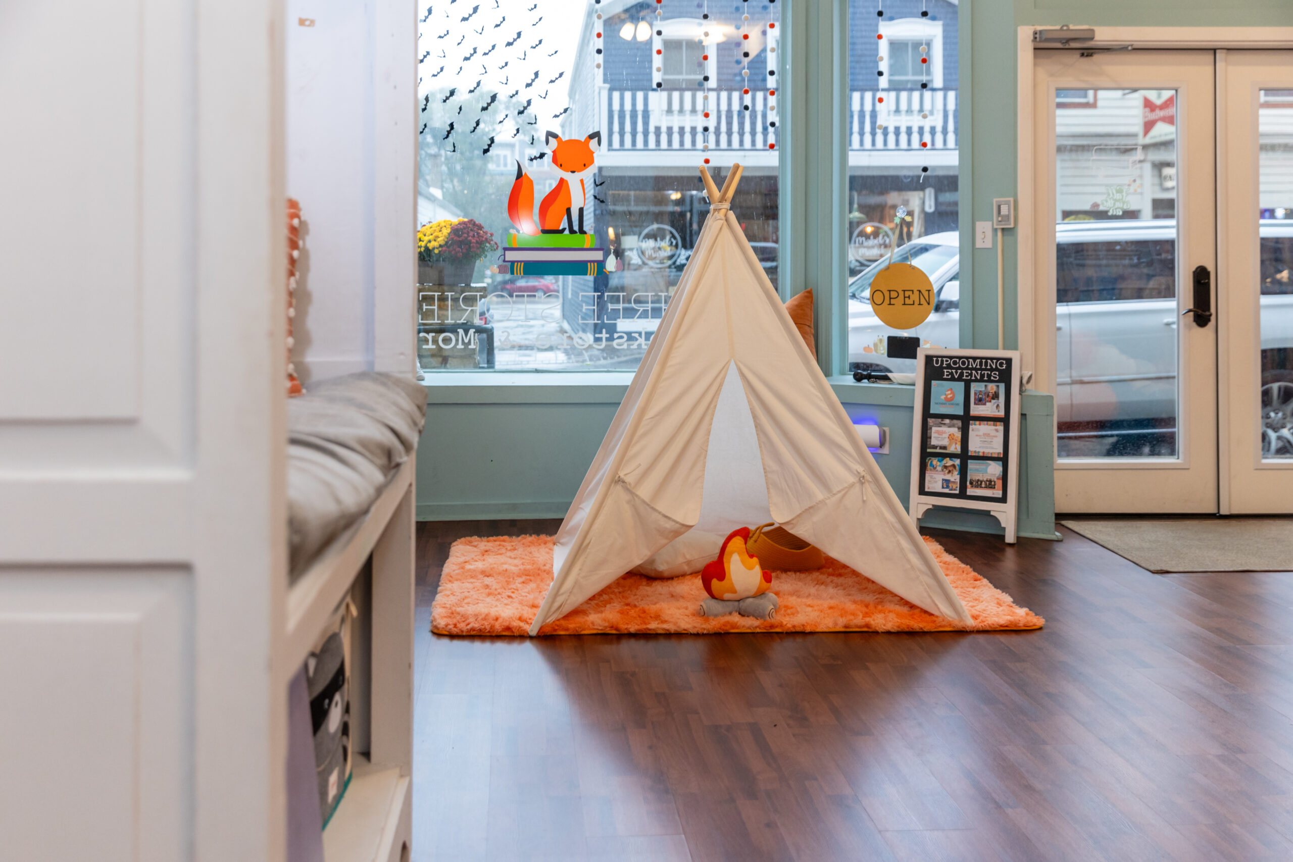 A children's play tent with an orange carpet is sitting on the ground in front of a large bay window 