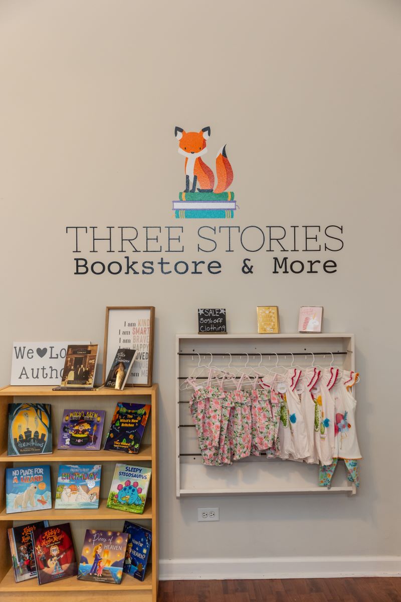 The name of the business is on the wall and there is a wooden bookshelf with books and a hanger with infant's clothing on display