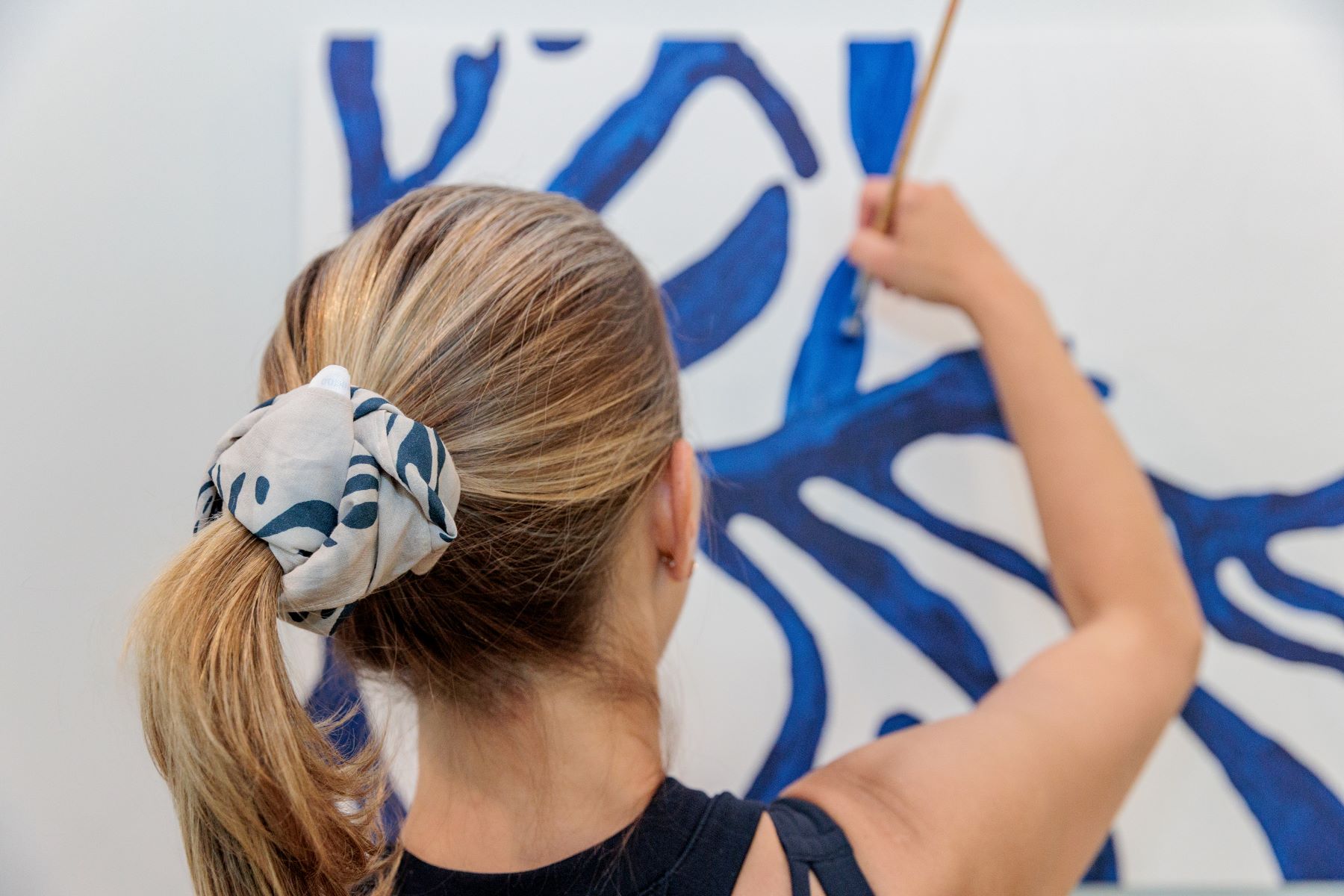 A woman in athletic wear with a scrunchie is painting on a wall with blue paint 