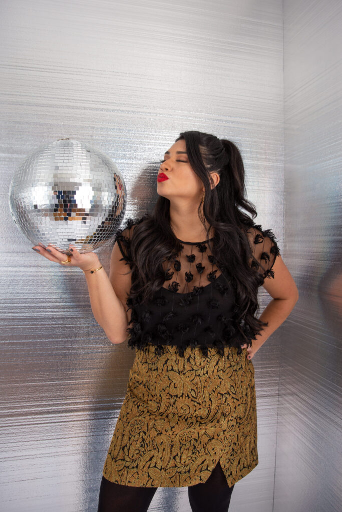 A person holding a disco ball in one hand and blowing it a kiss. 