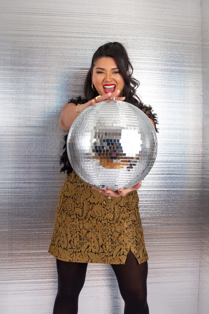 A person smiling and holding out a disco ball with both hands 