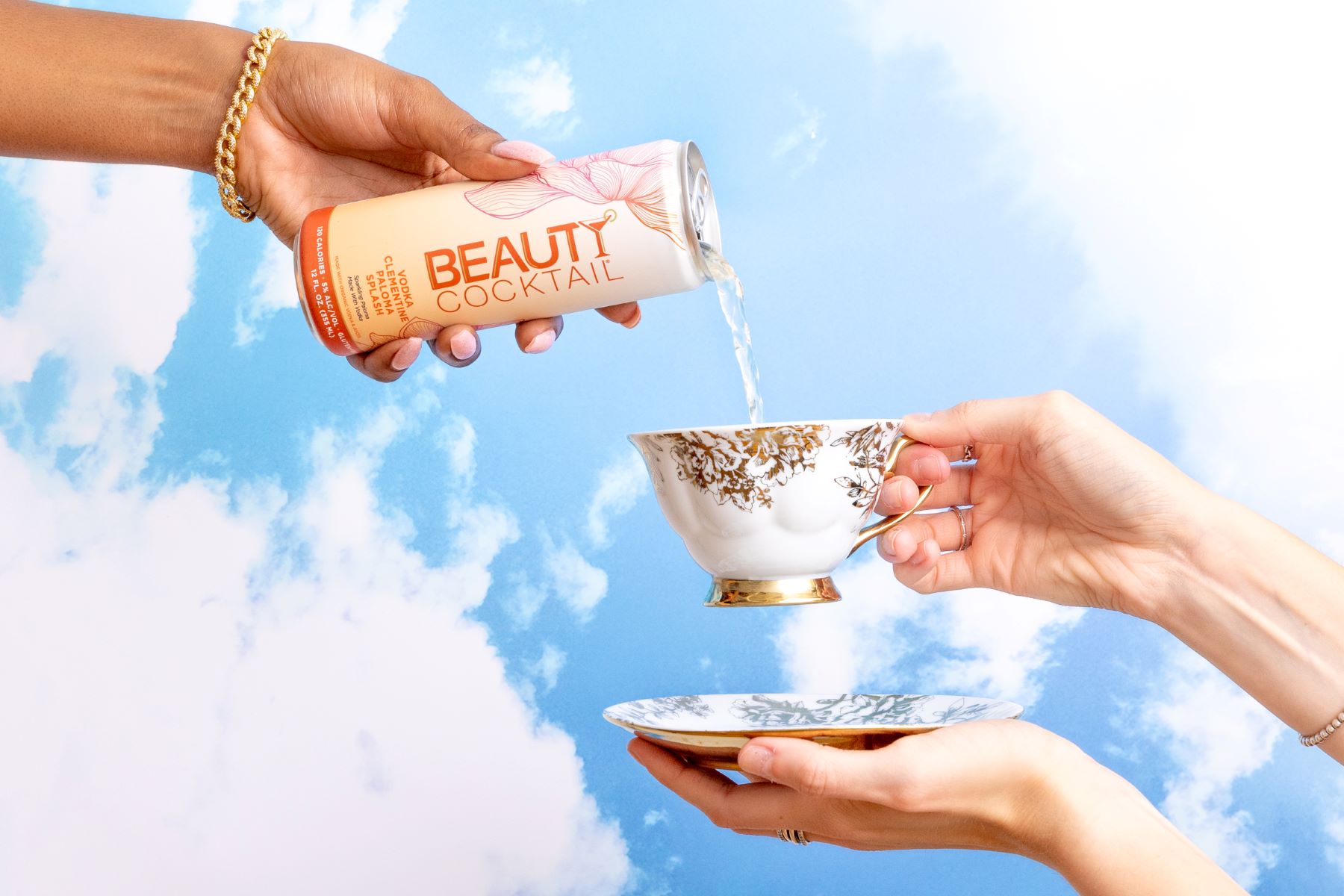 A drink being poured into a tea cup with a blue sky with white clouds as the background 