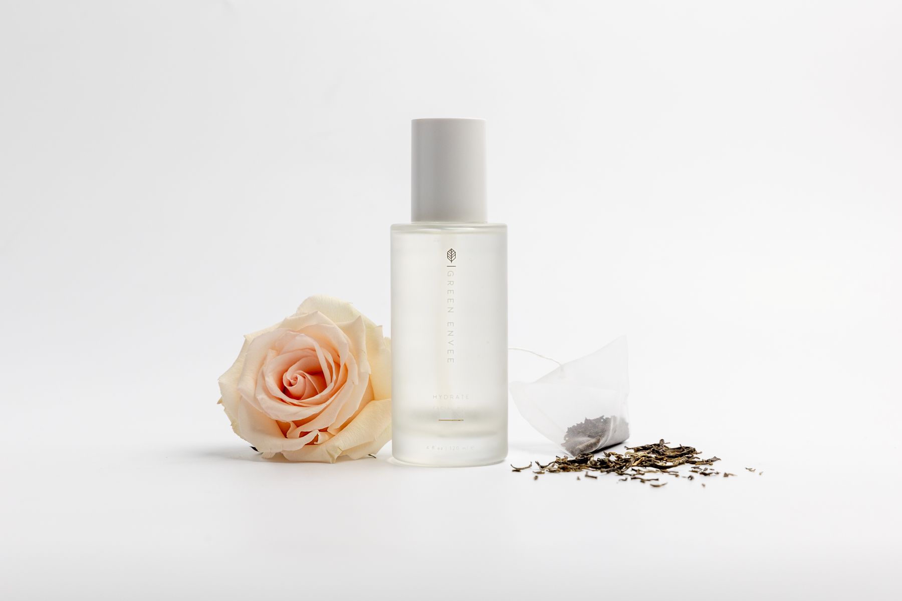 A clear white bottle with a skin care product next to it a rose 