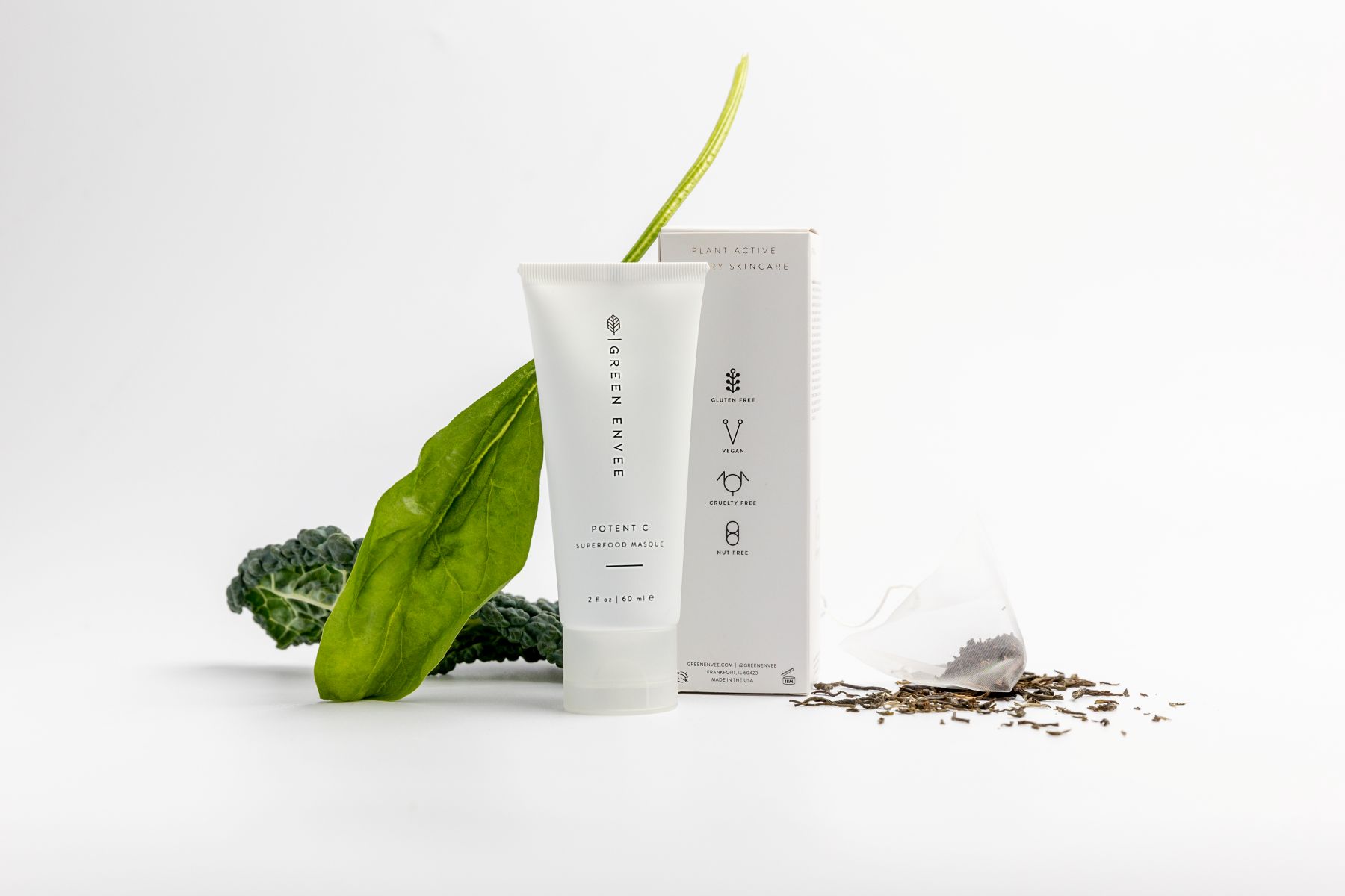 A white bottle with a cream for a face mask and a white box for the cream and next to it are plant leaves 