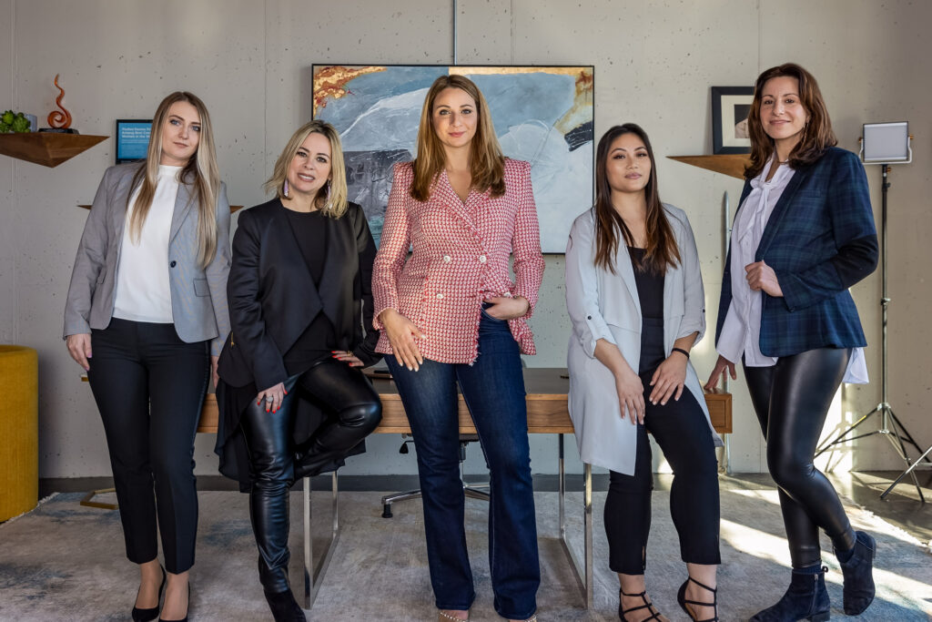Five people in business attire standing in front of a desk together smiling 
